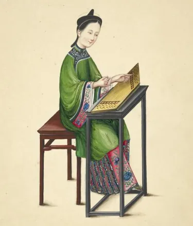 A woman in a green jacket sits on a stool and plucks a zheng zither laid on a tall black stand.