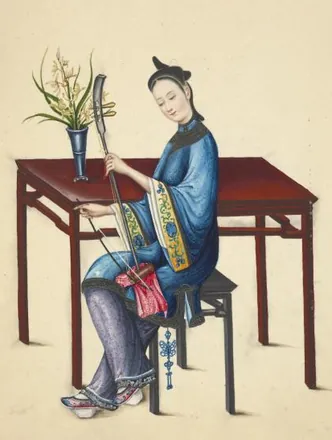 A woman in a blue jacket sits on a stool beside a red table and bows a small two-string jinghu fiddle held upright on her knee.