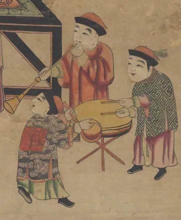Beside a lady standing at a table, three boys make music: one blows a long horn, one holds a small hand gong and one beats a drum on a stand.